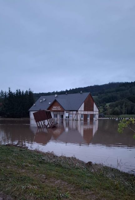 Budynek zalany wodą, charakterystyczny kontur odbija się w błotnistej tafli.