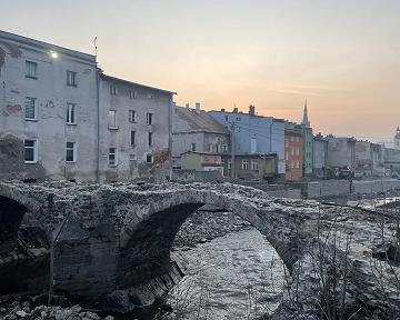 Kamienny most, nad rzeką, w tle stare kamienice i wieża kościoła.