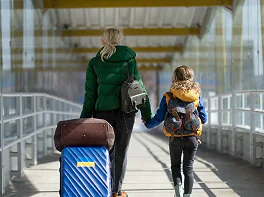 Kobieta z dzieckiem i bagażami idą przez zadaszone przejście.