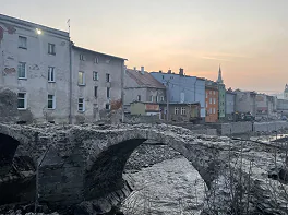 Kamienny most z łukami nad rzeką, w tle miasto z wielobarwnymi kamienicami.