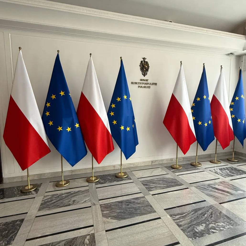 Naprzemiennie ustawione flagi Polski i Unii Europejskiej wewnątrz budynku Senatu Rzeczypospolitej Polskiej.