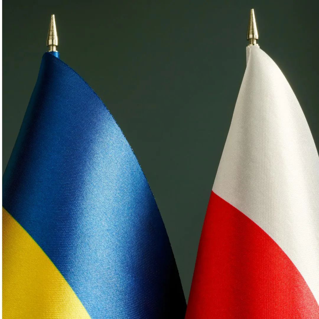 Małe flagi Ukrainy i Polski stojące obok siebie na ciemnym tle.